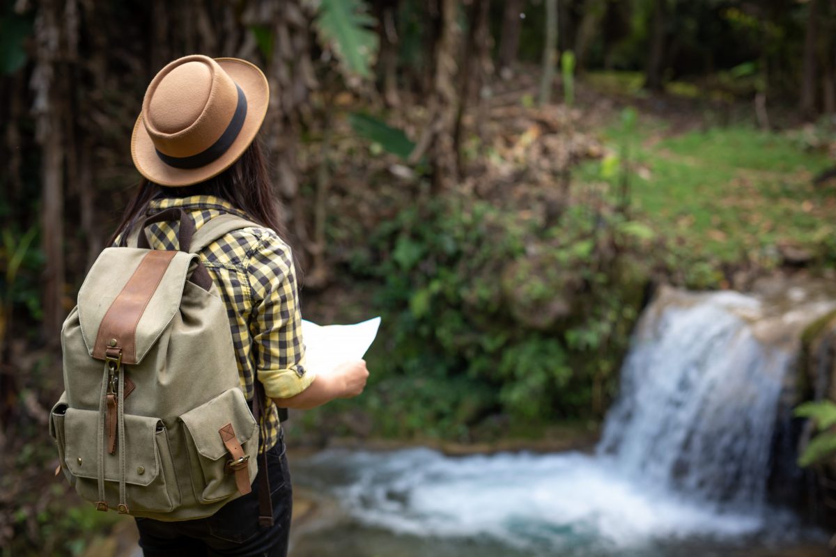 Turismo sostenibile: ragazza che va all'avventura con zaino e cartina, davanti ad una cascata